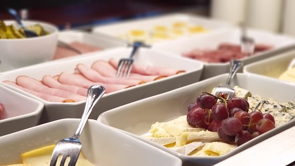 A close up of platters with different cheeses, meat and grapes.