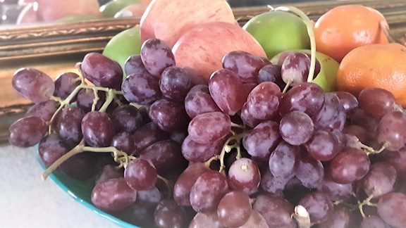 Grönt fat med lila vindruvor, äpplen och apelsiner.