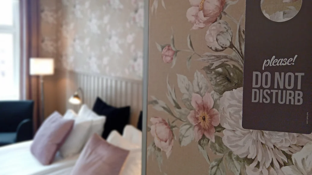En närbild på en Stör Ej-skylt, med en säng i bakgrunden.