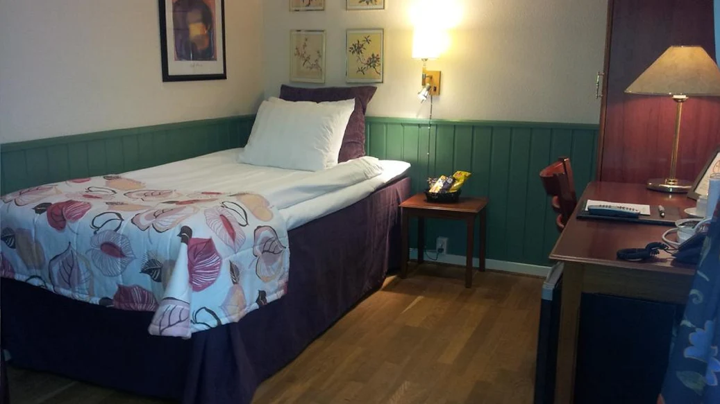 Enkelrum med panelklädd vägg och säng bäddad med vita, krispiga lakan.