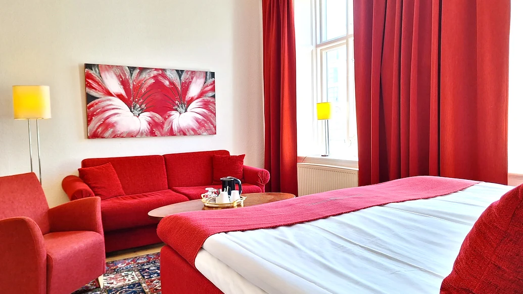 Ett hotellrum med en röd soffgrupp framför en röd säng med vita lakan.