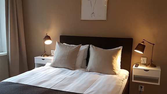 A small double bed with crisp white sheets in a room with beige walls.