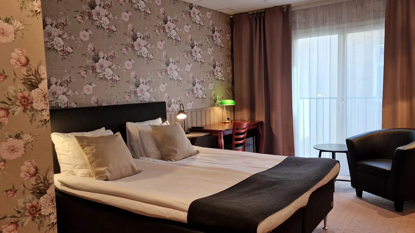 Ett dubbelrum med blommiga tapeter, en dubbelsäng, läderfåtölj och en fransk balkong.