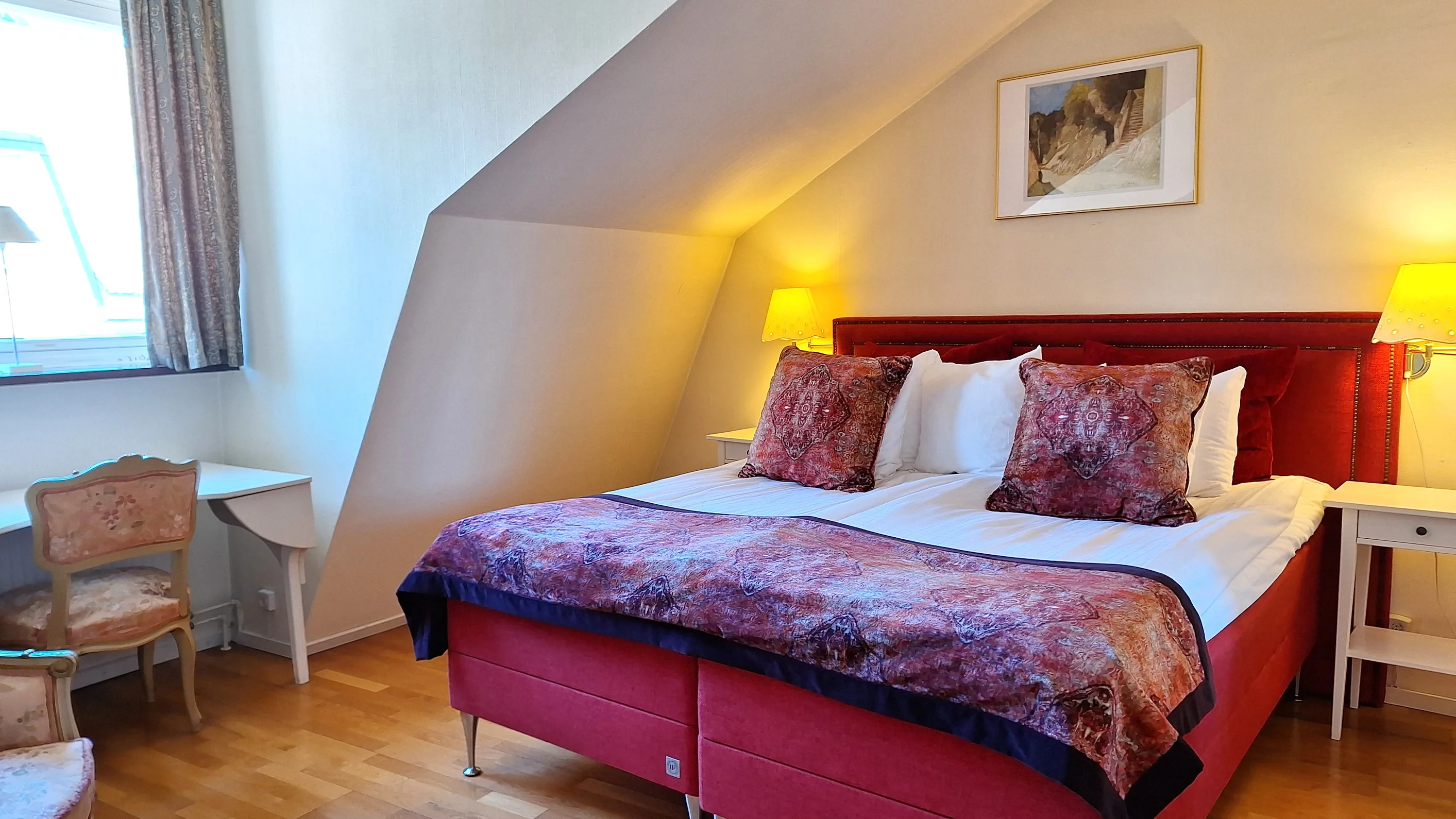 Ett hotellrum med vita väggar och en stor röd dubbelsäng med vita lakan och röda prydnadskuddar och överkast.