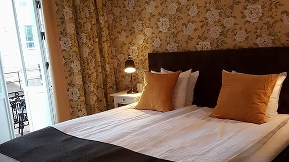 A double bed in a room decorated with yellow wallpaper with flower motifs and a balcony out to the street.