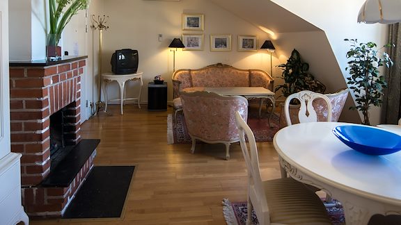 A spacious room with a dining room set, a pink sofa and two armchairs with a fireplace to the side.