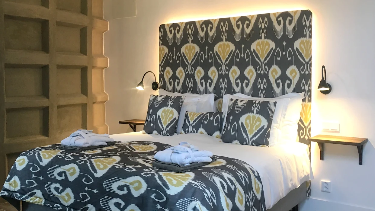 En säng med vita lakan, prydnadskuddar och överdrag i samma blå färg med vitt och gult mönster.