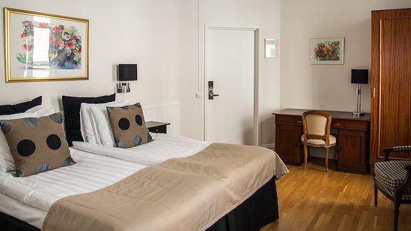 A white room with a double bed, wooden floors and a small desk.