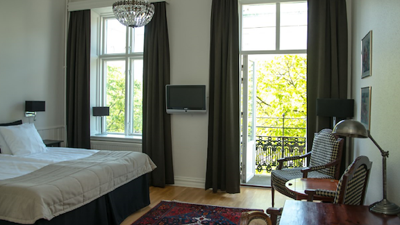 A room with a double bed, a chandelier, two armchairs and a balcony facing the street.