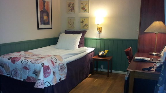 A single bed with crisp white sheets and a desk to the side.