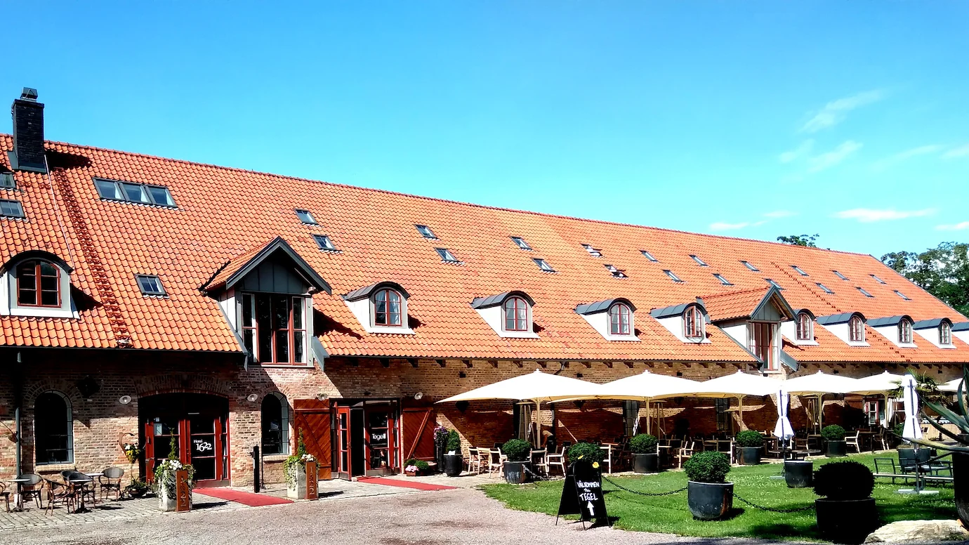 En lång, brun tegelbyggnad med entré till Hotel 1622 och Restaurang Tegel bredvid varandra, en solig dag.