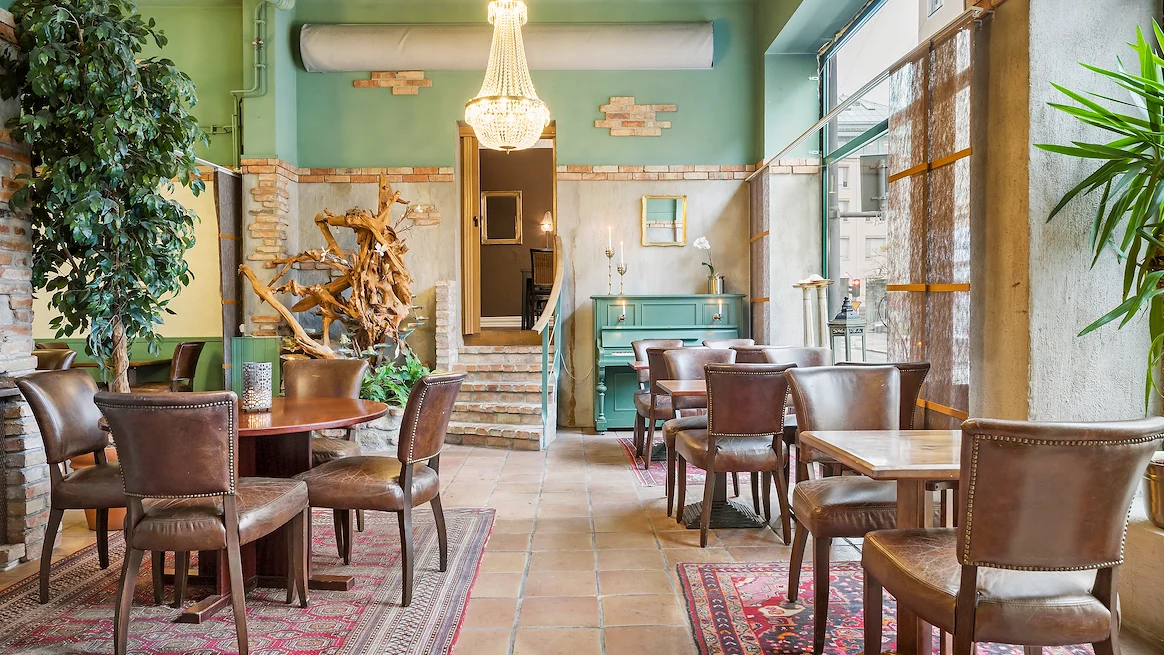 The hotel breakfast room. A bright room with tall ceilings, a chandelier, brown tables and chairs.