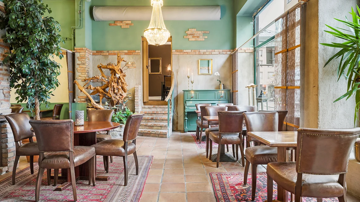 Hotell Linnéas frukostmatsal. Ett ljust rum med högt i tak, en kristallkrona, bruna bord och stolar.