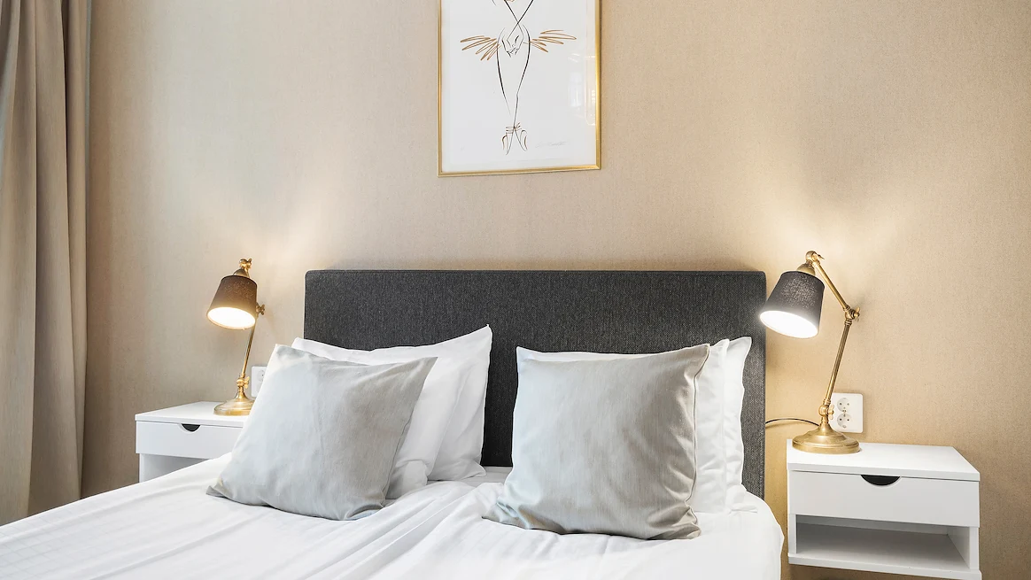 En mörkgrå dubbelsäng med vita lakan och grå prydnadskuddar.