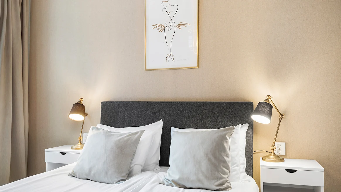 A small double bed with crisp white sheets in a room with beige walls.