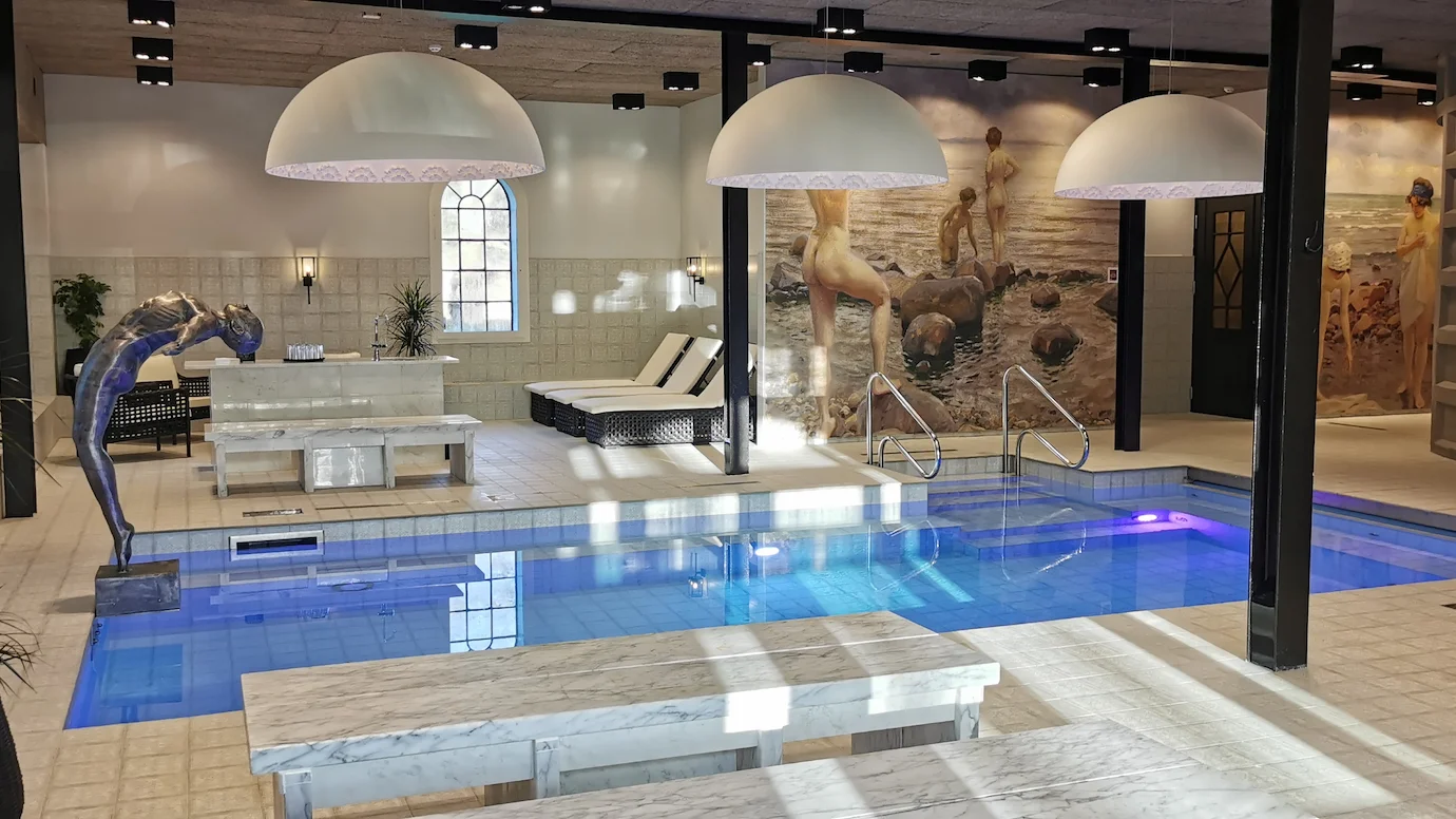 Ett rum med vitt kakel och en stor simbassäng i mitten, med en staty av en kvinna som dyker baklänges i ena änden.
